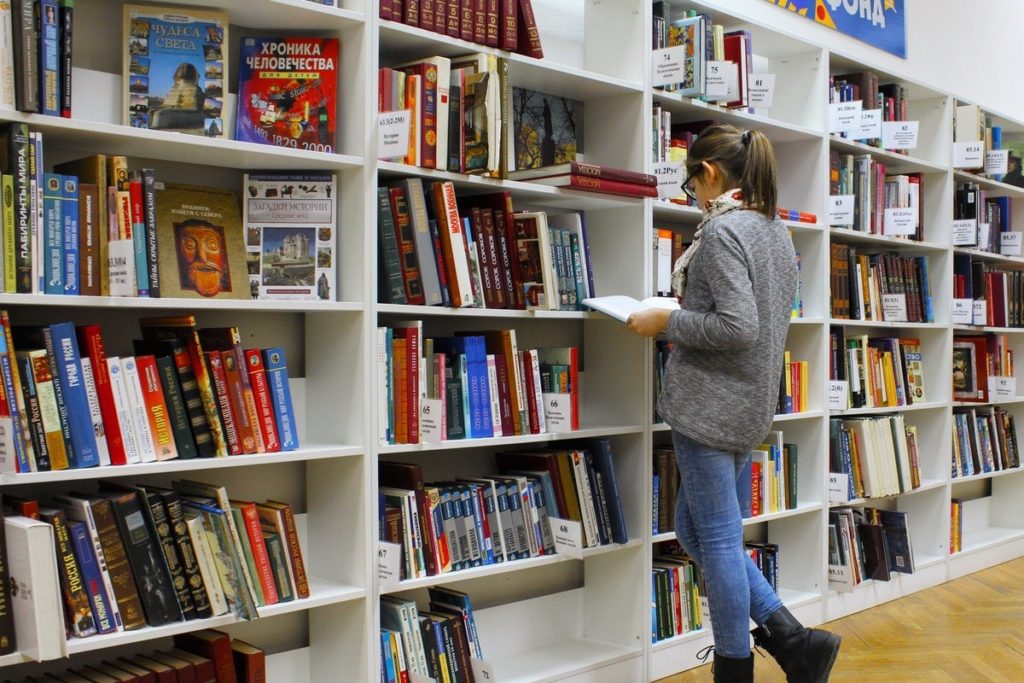 Student reading a book in front of a bookshelf in a library in Australia.