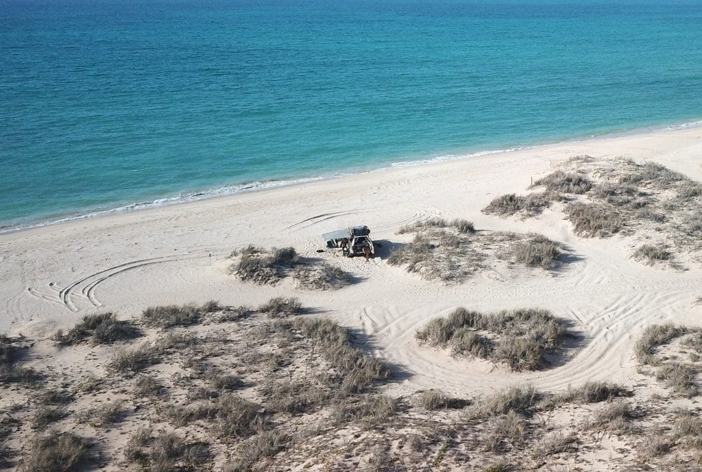 4WD on the middle of the beach with white sand and clear blue waters in Exmouth in western Australia.